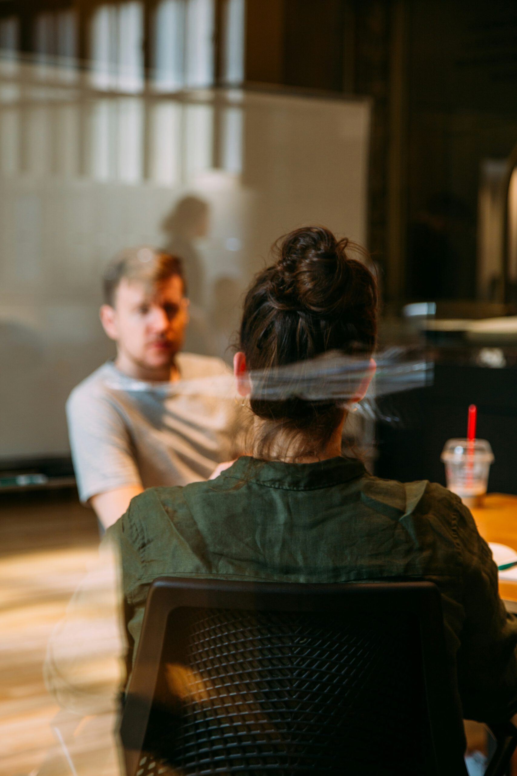 Zwei Personen im Gespräch an einem Bürotisch, eine Mitarbeiterin von hinten – Austausch mit einer Fachperson (Beitragsbild)