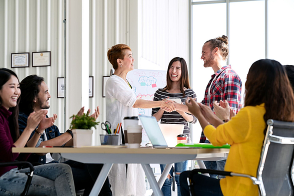 Begrüssung per Handschlag in einem Büro, das Team applaudiert – Beitragsbild Rekrutierung